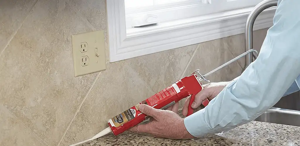 Handyman applying caulk along a kitchen backsplash and countertop seam in Huntsville, AL