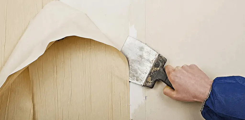 Handyman removing wallpaper with a scraper for wall preparation in Huntsville, AL